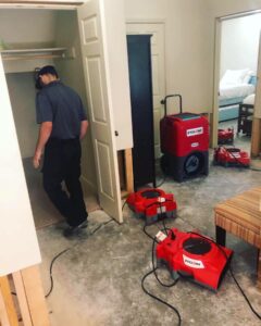 Technician operating red air mover and dehumidifier in a water-damaged room