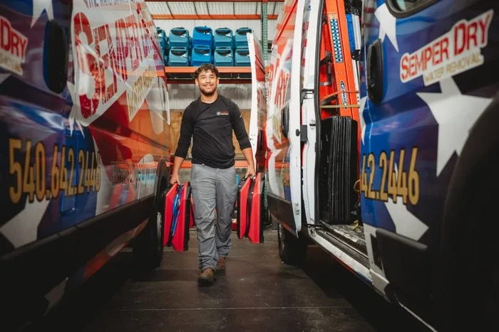 Semper Dry technician carrying drying equipment between two branded water removal vans