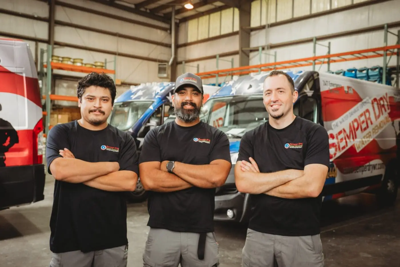 Three IICRC certified Semper Dry restoration technicians standing in front of patriotic wrapped service vans in the Virginia warehouse